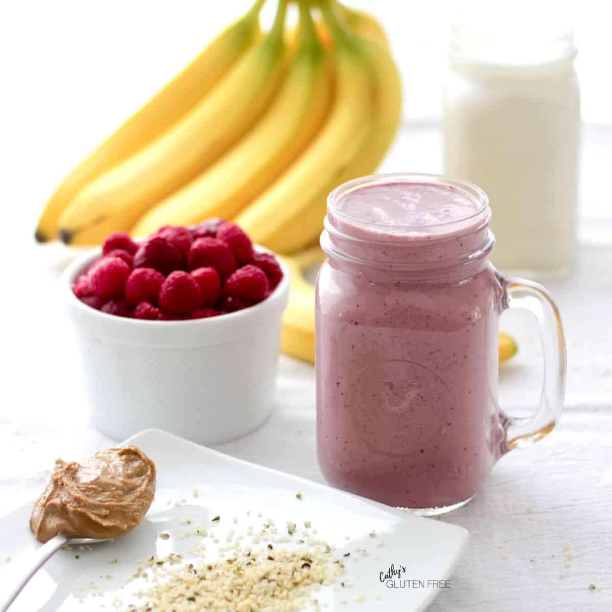 pink smoothie in a glass with a handle, and bananas, berries, and nut butter.