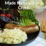 raw sauerkraut on black plate with sausage, lettuce, and red onion.