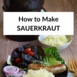 sauerkraut on black plate with sausage, salad, more raw sauerkraut, and crock in background.