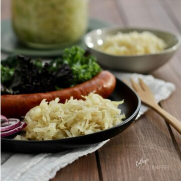 sauerkraut on black plate in front of sausage and greens with jar in background