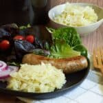 raw sauerkraut on a black plate with sausage and salad.