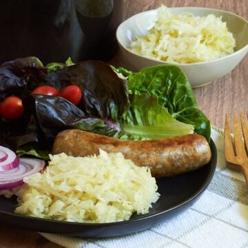 raw sauerkraut on a black plate with sausage and salad.