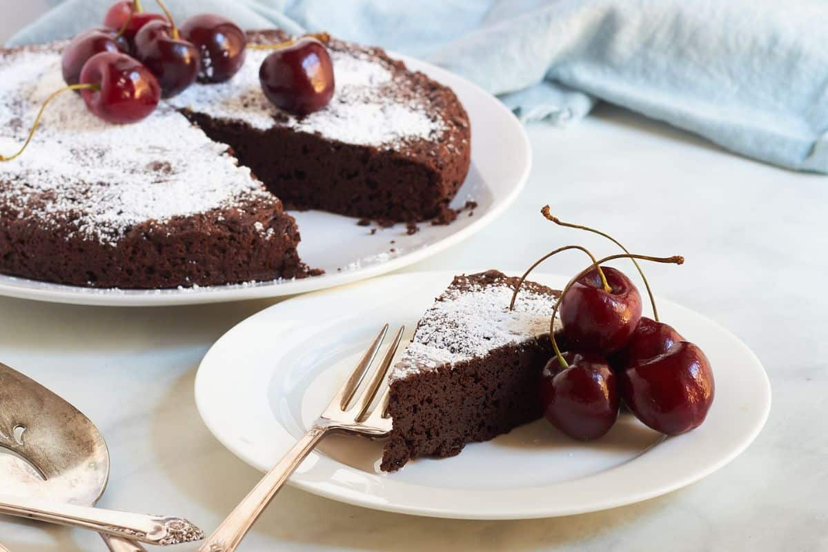 flourless chocolate cake with a wedge served on a white plate, garnished with fresh cherries.