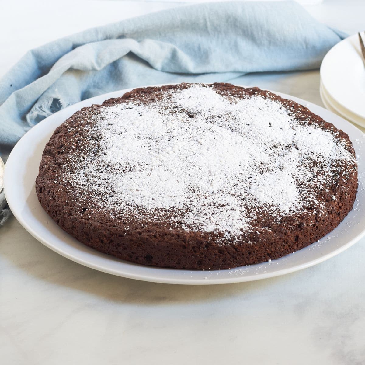 round chocolate cake on white plate, dusted in white.