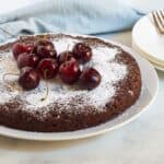 round single-layer chocolate cake dusted in white and topped with fresh cherries.