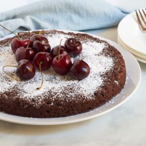 round single-layer chocolate cake dusted in white and topped with fresh cherries.