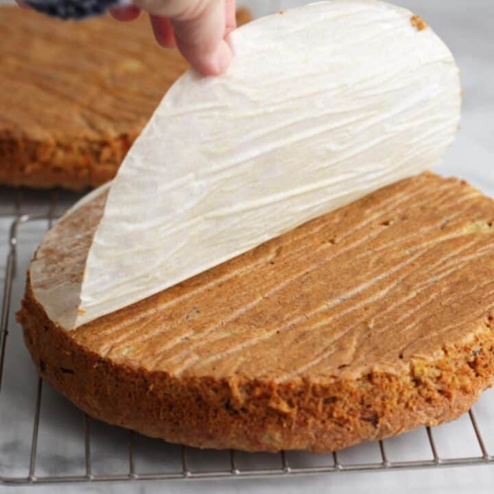 parchment paper being peeled from round cake layer on wire cooling rack