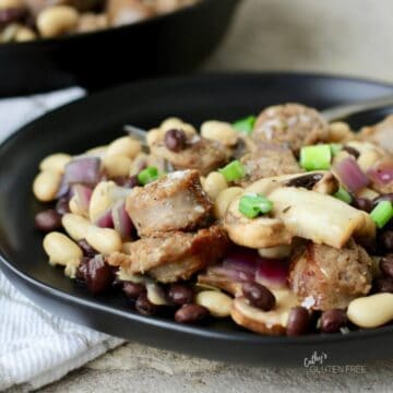 chunks of cooked sausage, sliced mushrooms, chopped red onion, and beans on a black plate.