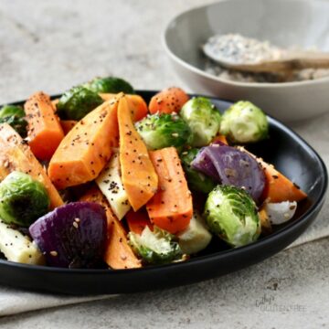 roasted carrots, Brussels sprouts, and red onion sprinkled with coarse seasoning on black plate
