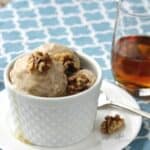 round scoops of ice cream in a white dish, topped with walnuts and maple syrup dripping down the side