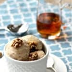 scoops of ice cream in a white bowl with walnuts on top and maple syrup drizzling down the side