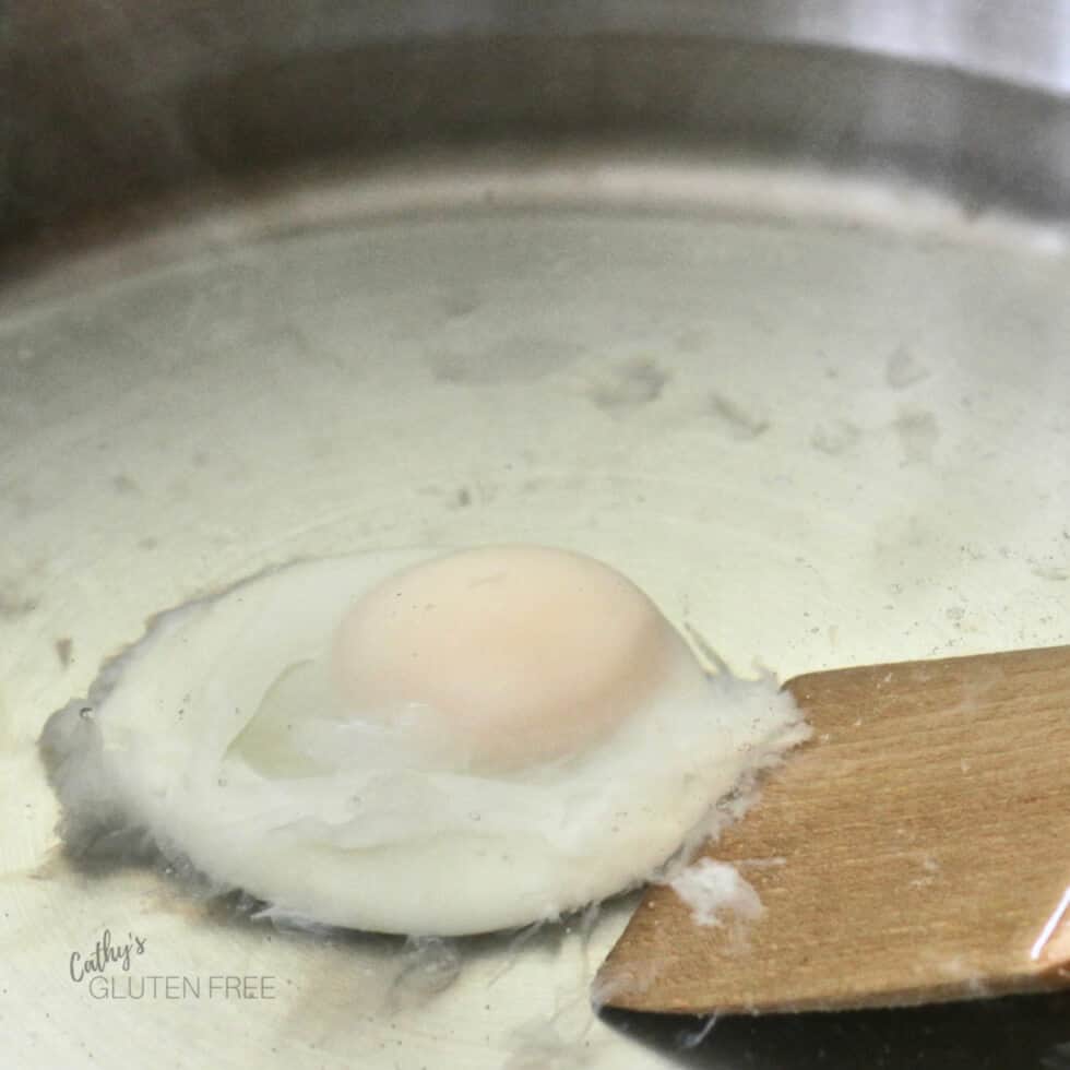 a wooden lifter scoops under a softly poached egg in water