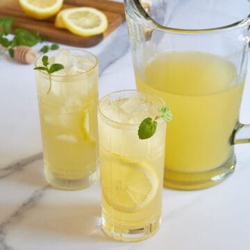 two glasses of lemonade garnished with mint beside a pitcher of lemonade.