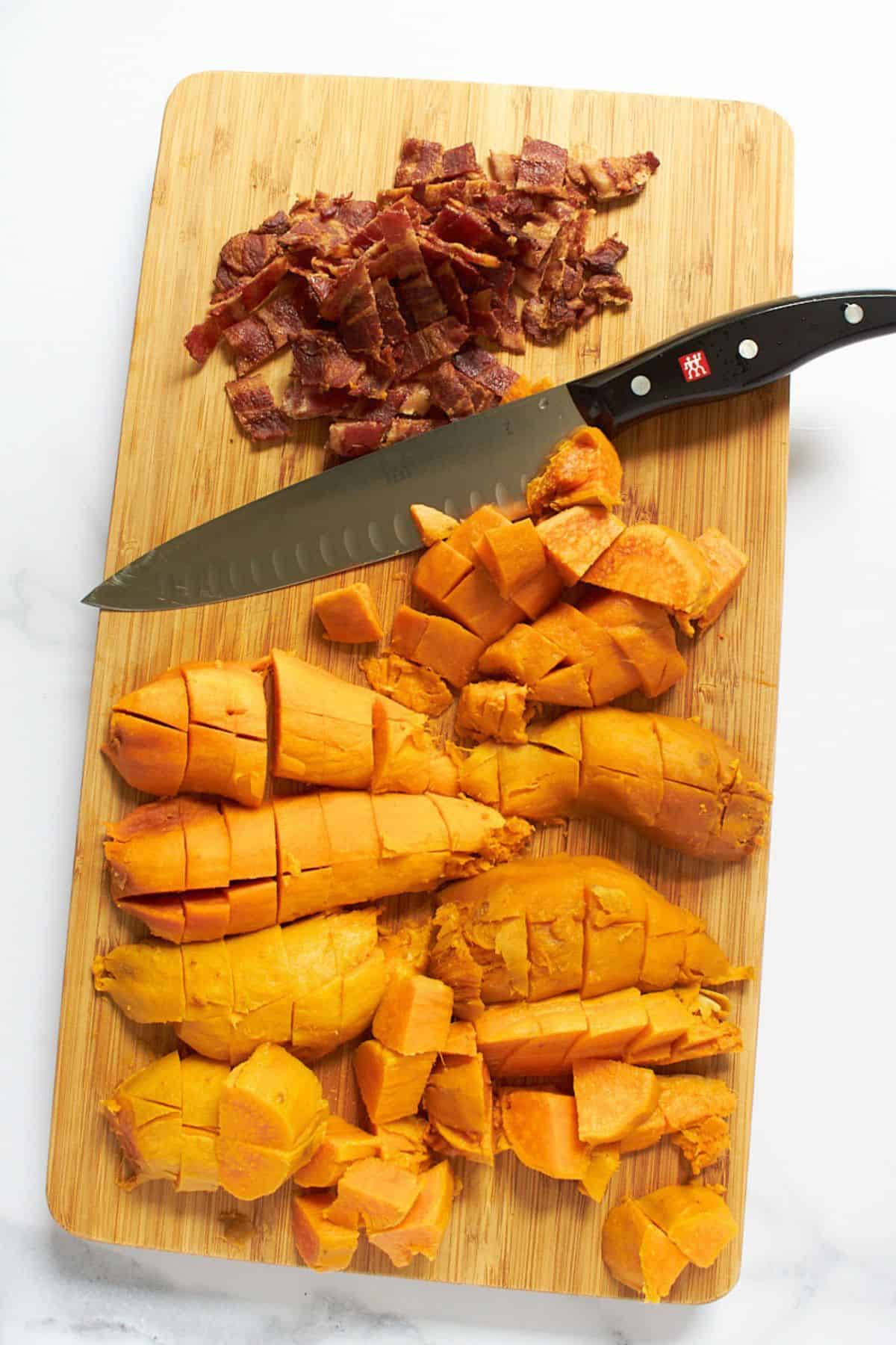 chopped, cooked bacon and sweet potatoes on bamboo cutting board with knife.