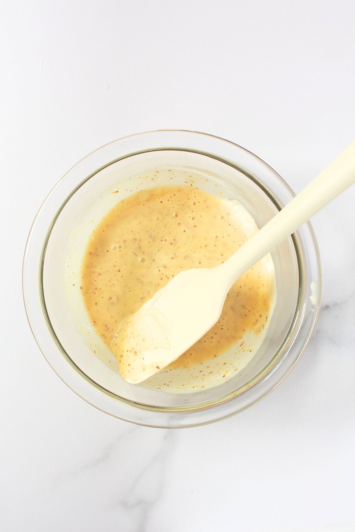 creamy dressing in a glass bowl with a spatula.