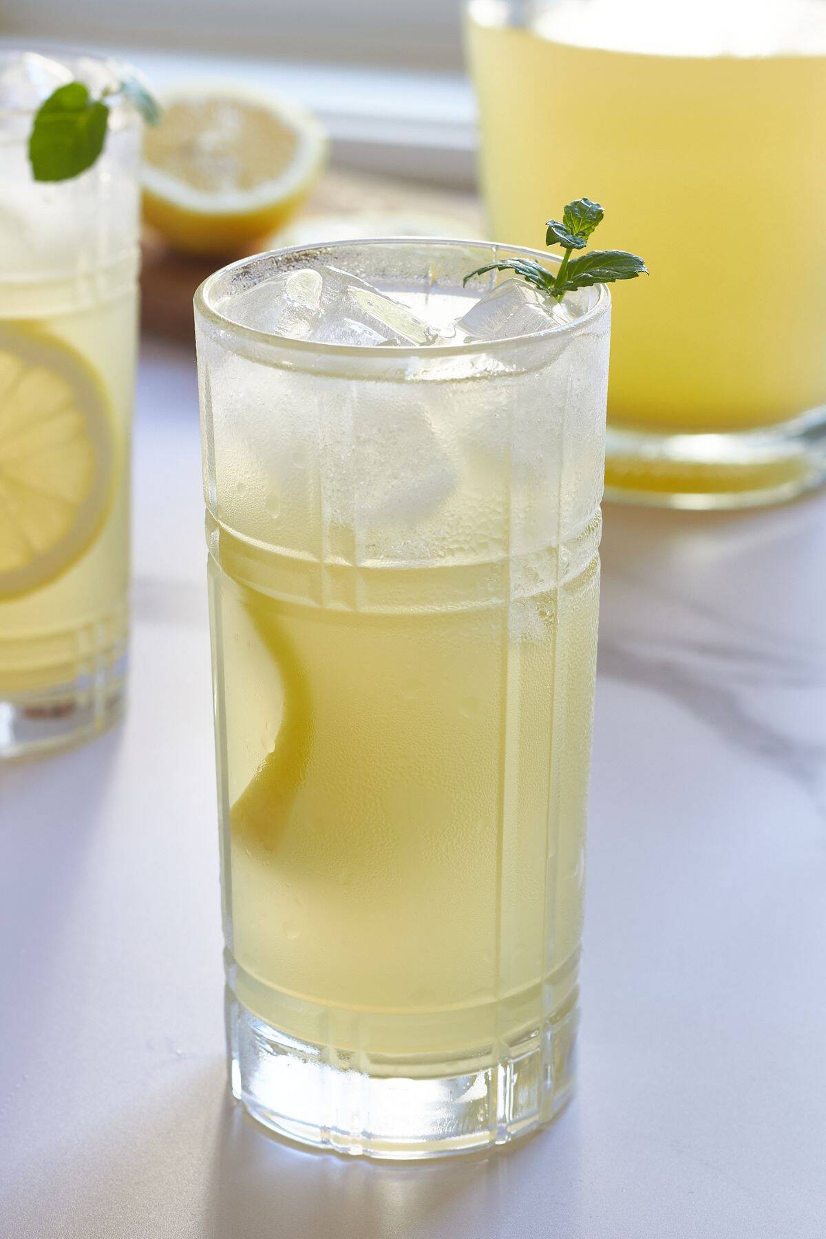 closeup of glass of lemonade with ice, slice of lemon, and sprig of mint.