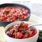 chili with ground meat and chunks of tomato in white bowl, more in black bowl in background