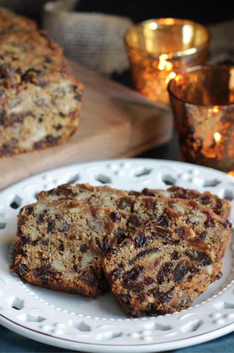 sliced fruitcake on a white Christmas plate, with golden candles.