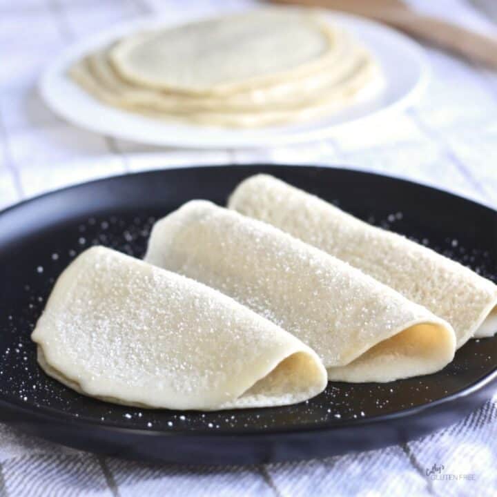 three folded crepes arranged overlapping on a black plate, with more stacked in background