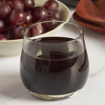 clear glass bowl of dark, balsamic vinaigrette with red grapes in background.