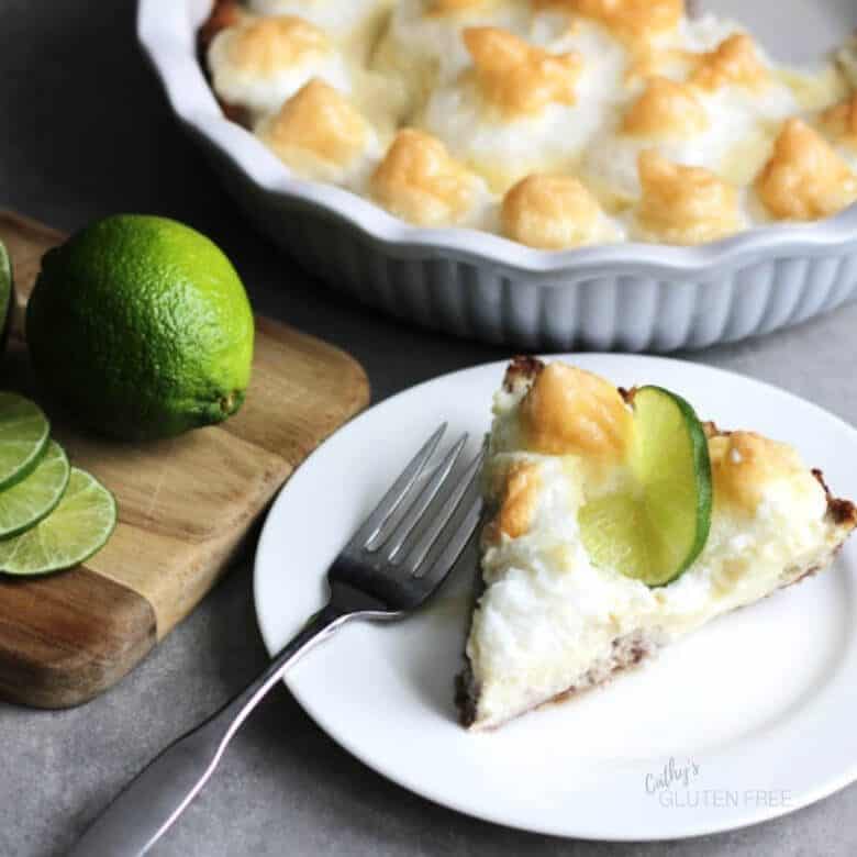Slice of meringue-topped pie on white plate, meringues and pie in background