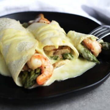 Gluten Free Seafood Crepes with shrimp, asparagus and hollandaise sauce on black plate