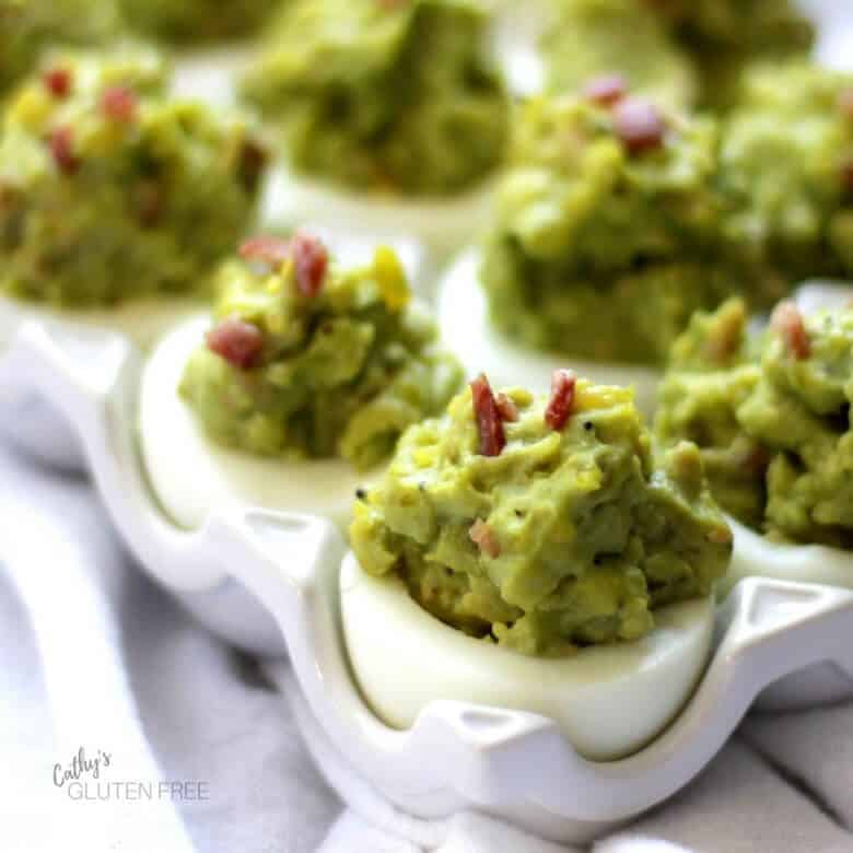 close up of green, avocado deviled eggs garnished with bacon bits