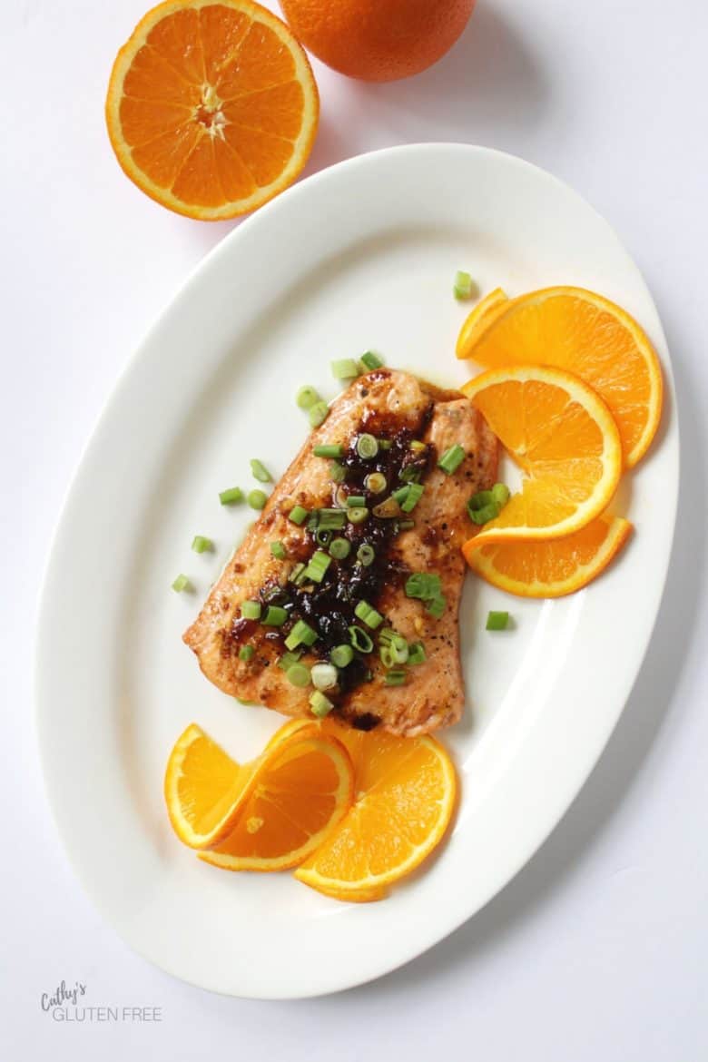 top-down view of salmon with green onion and orange slices served on an oval white platter