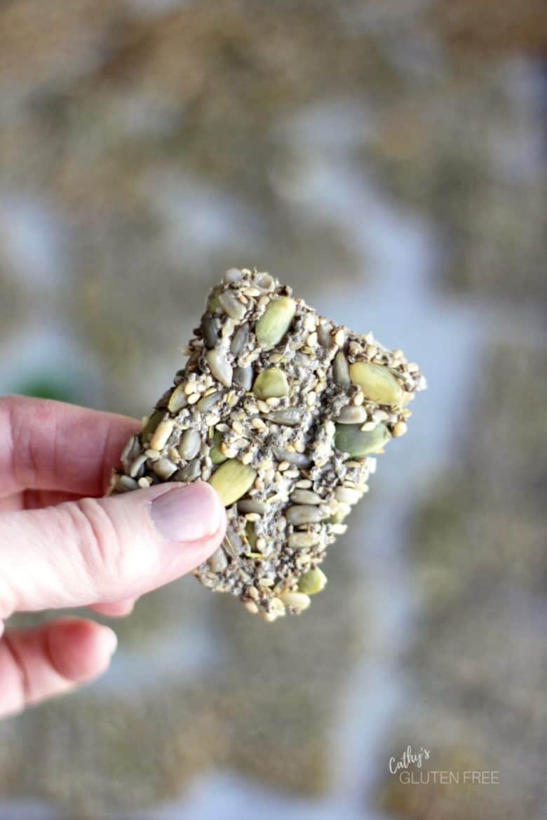 single cracker with pumpkins seeds is held up between fingers