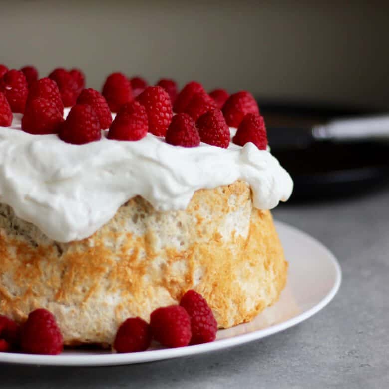 angel food cake, made with gluten free flours, topped with whipped cream and raspberries