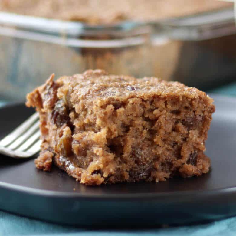 a square of moist applesauce cake sits on a dark plate with a fork beside it