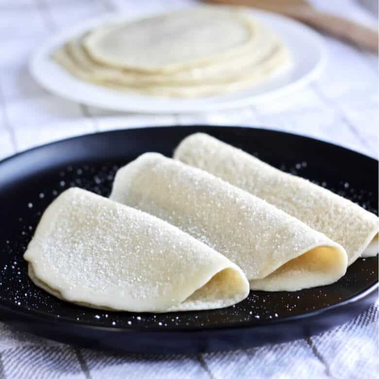 three crepes, made with gluten free flours, folded on a black plate