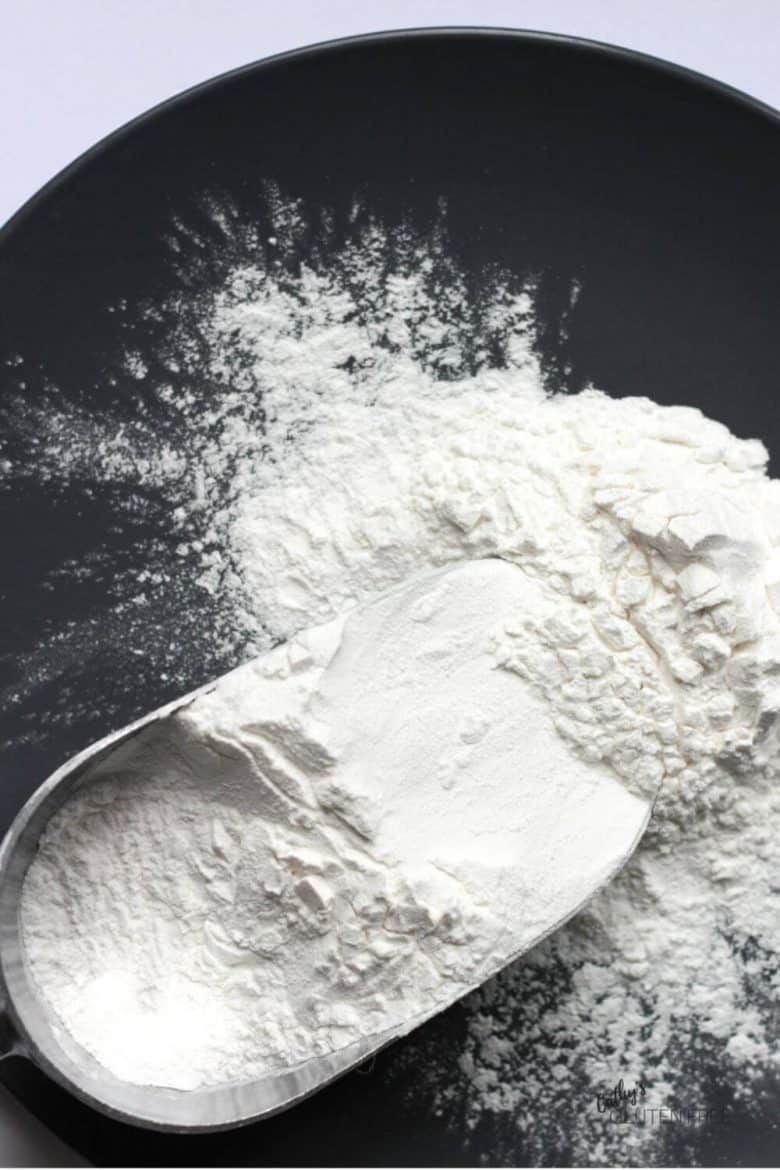white gluten free flour spills onto a black background from a scoop