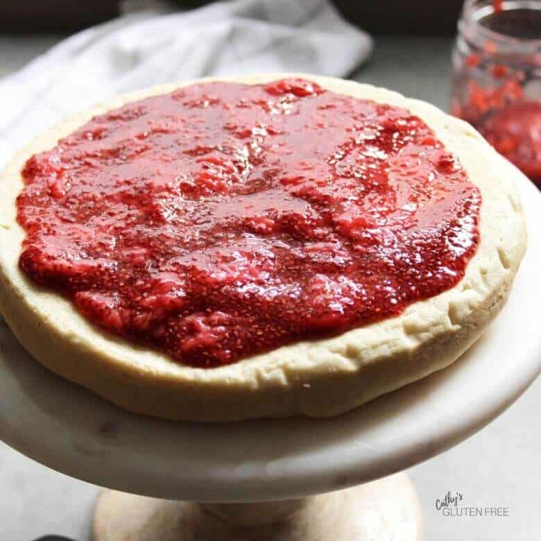 strawberry jam spread over a single layer of vanilla cake on a pedestal plate