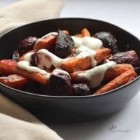 roasted beets and carrots, drizzled with yogurt, in a black bowl