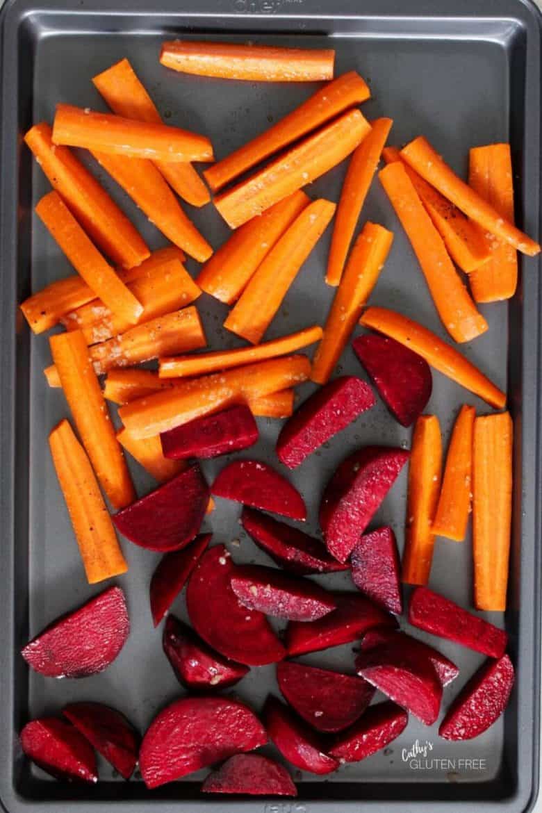 carrots and beets spread out on a baking pan ready to be roasted