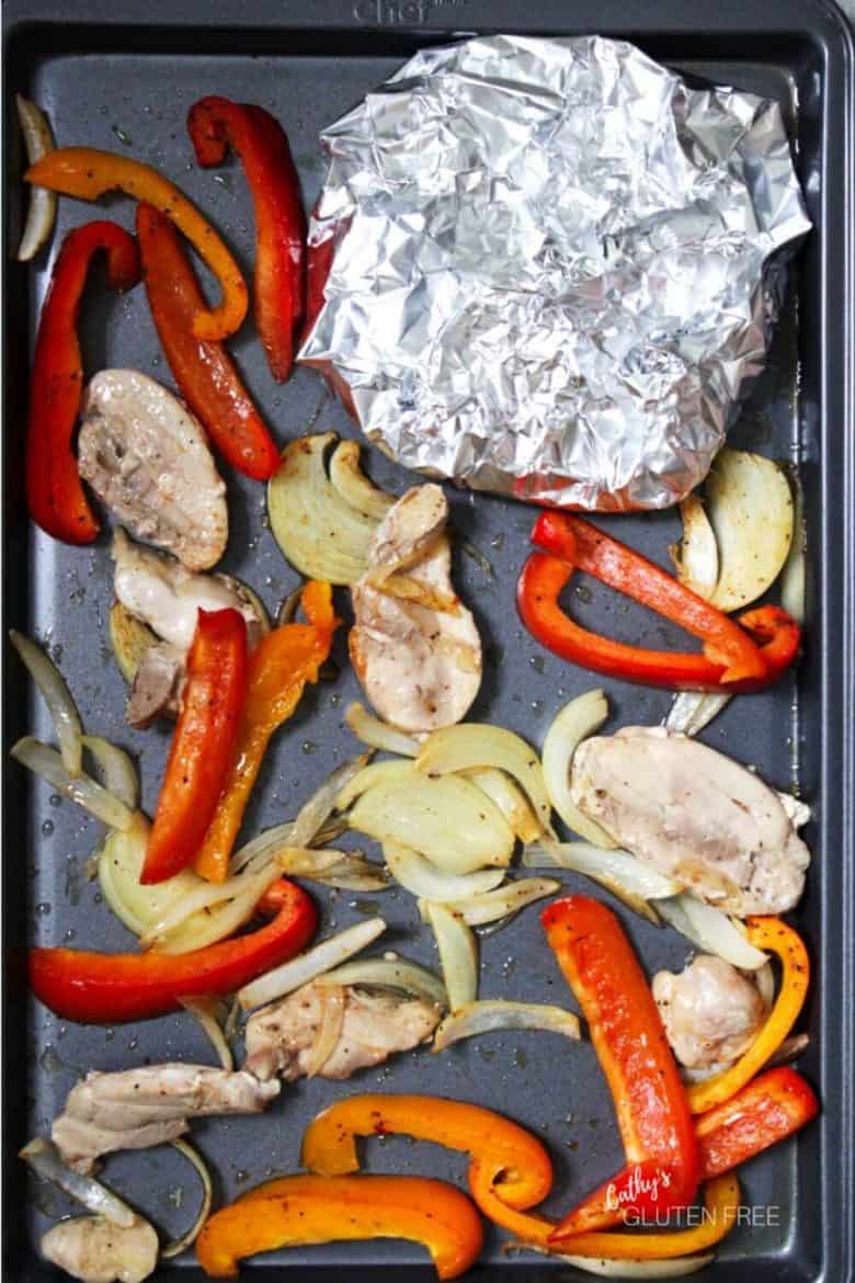 foil wrapped tortillas tucked into the corner of sheet pan with vegetables and meat