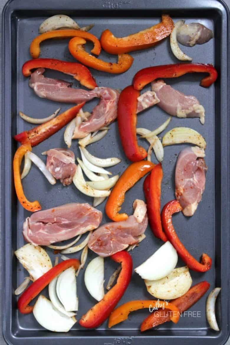 raw peppers, onions, and chicken strips spread over a baking sheet