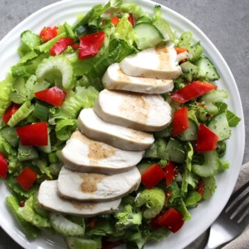 slices of cooked chicken spread over white plate of fresh salad greens and drizzled with salad dressing.