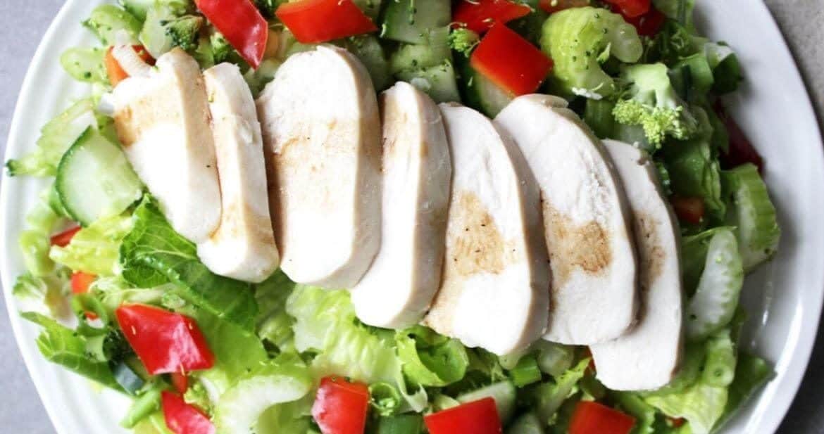 sliced cooked chicken laid across a lettuce salad