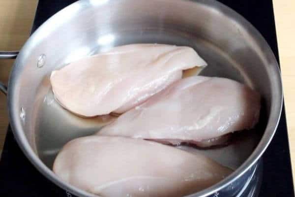 three raw chicken breasts in stainless pan