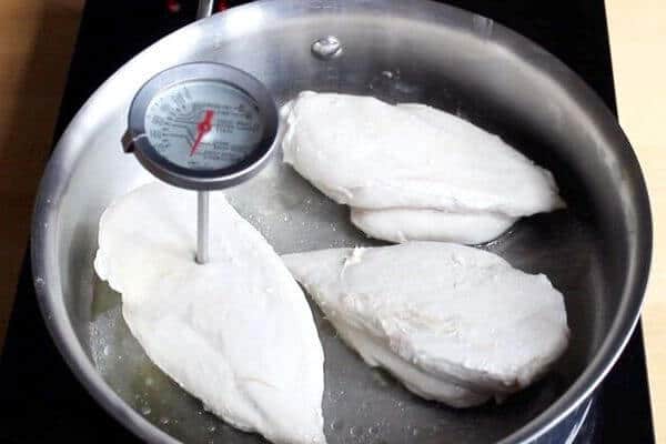 Three cooked chicken breasts in stainless steel pan with meat thermometer inserted in one