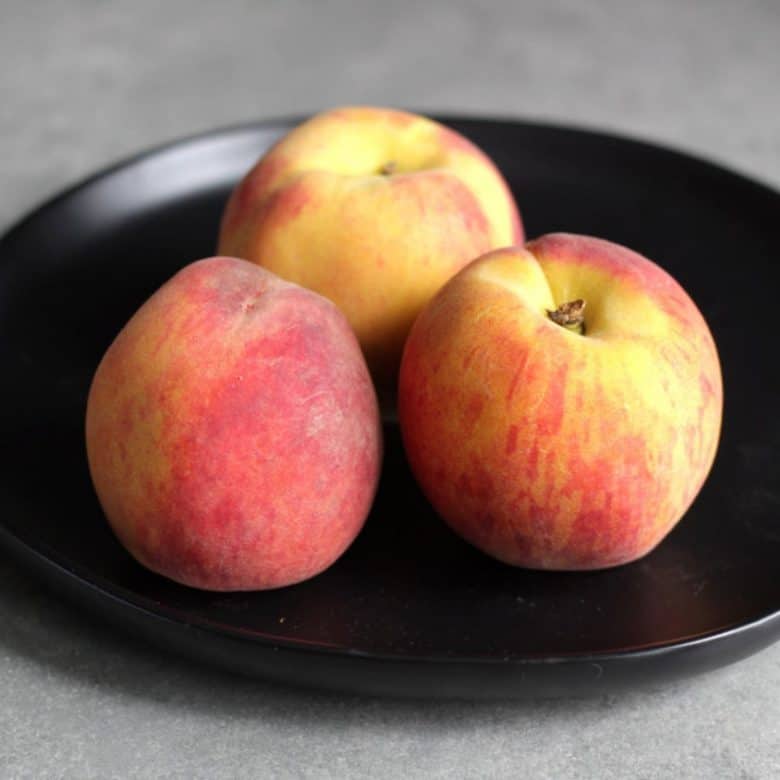 three fresh peaches on black plate