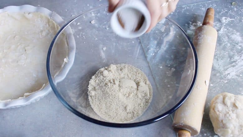 spices being poured into raw sugar in a clear glass bowl