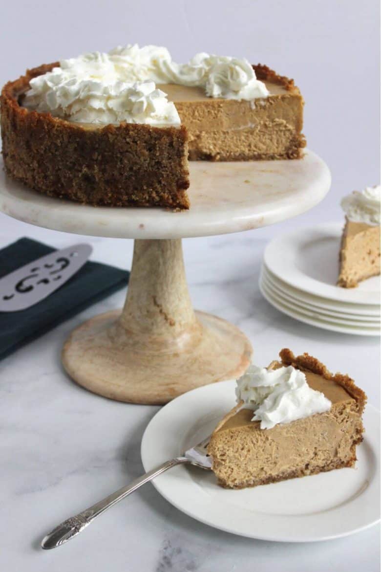 two slices of gluten free cheesecake recipe with pumpkin served on white plates with remaining cake on marble pedestal