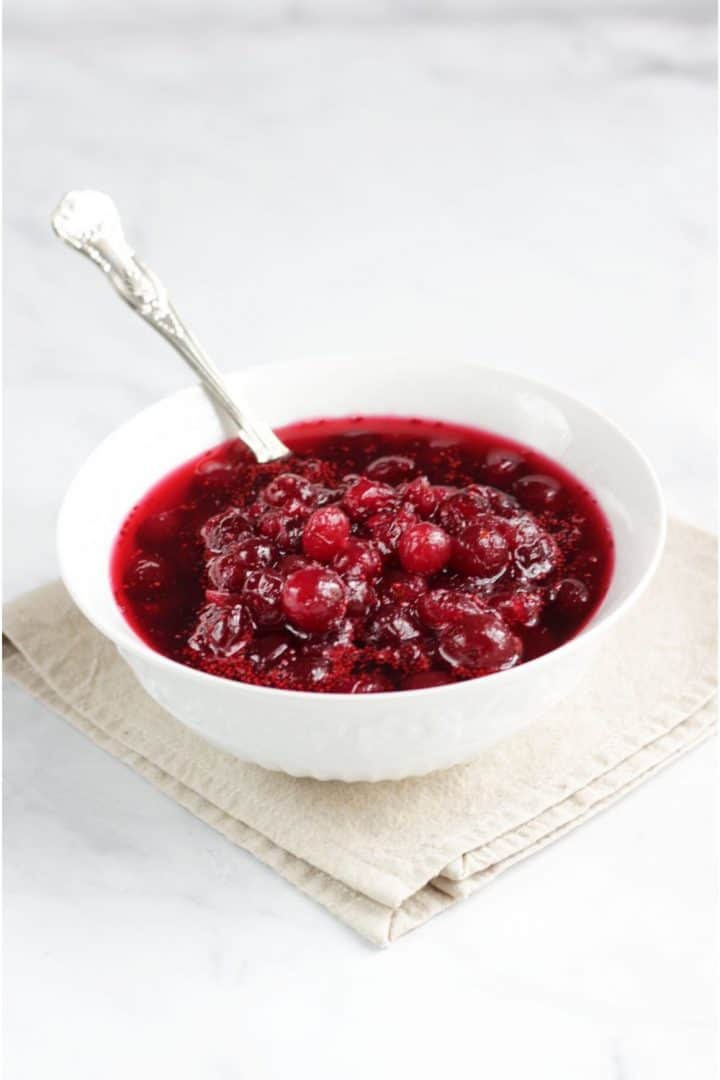 rich, red cranberry sauce in white bowl with silver spoon 