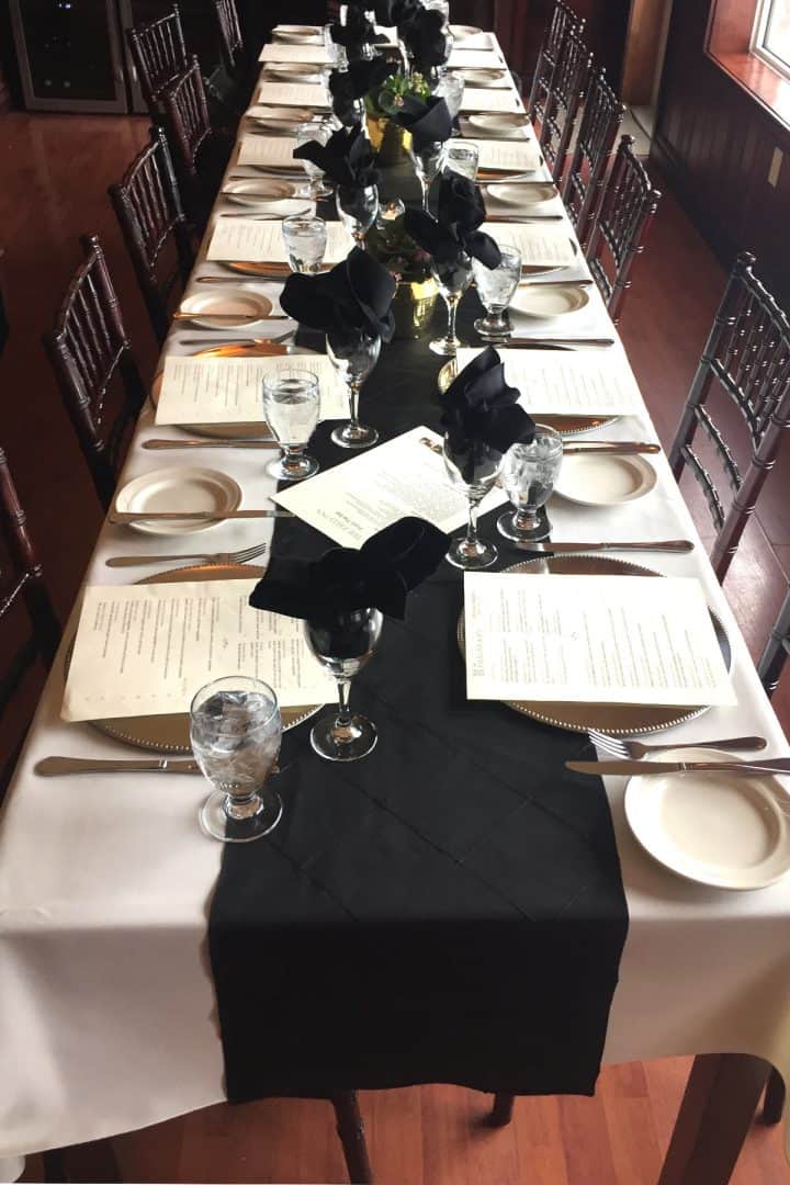 long table with white tablecloth and black runner, set for dinner