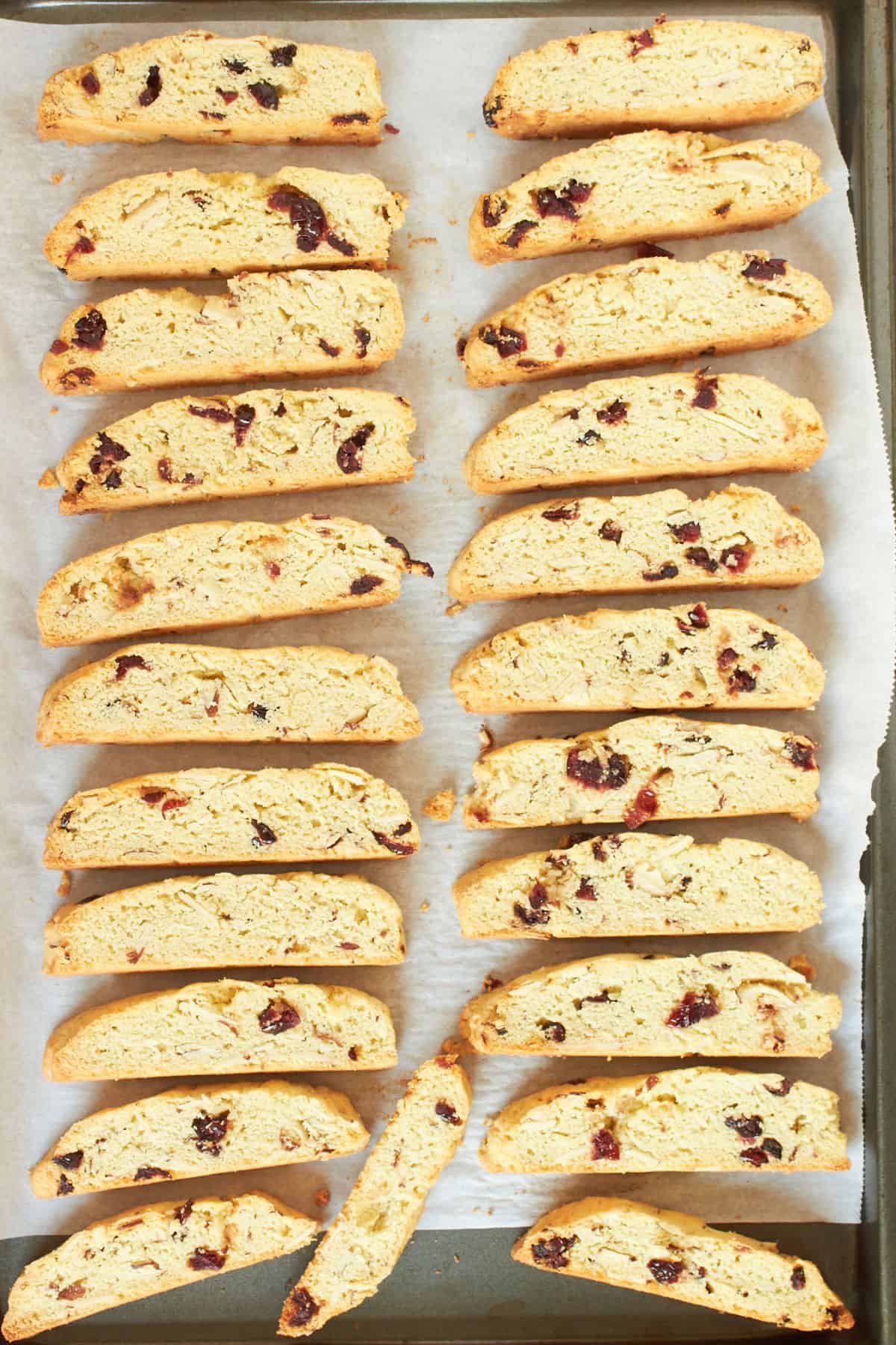 sliced toasted gluten-free cranberry biscotti spread out on parchment-lined baking sheet.