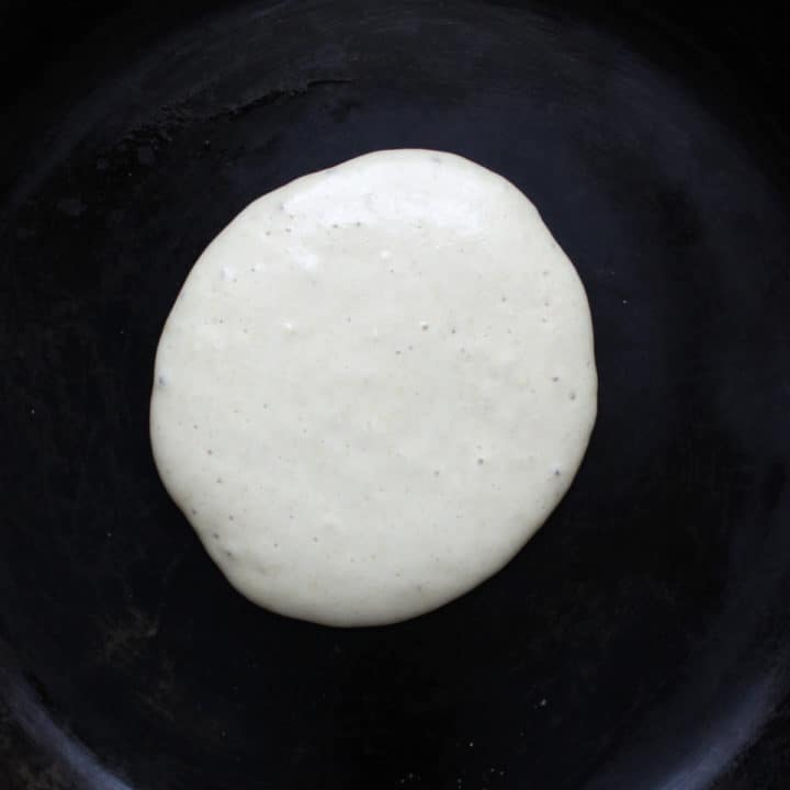 pancake cooking in pan with small bubbles on top