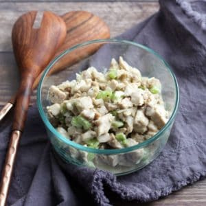 chicken salad with celery in glass bowl on lavender napkin with wooden spoons